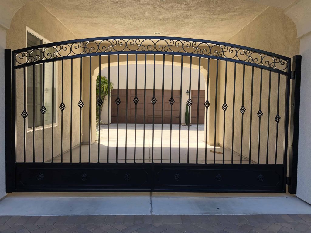 Single swing iron driveway gate with an arched top and finials hung from one post
