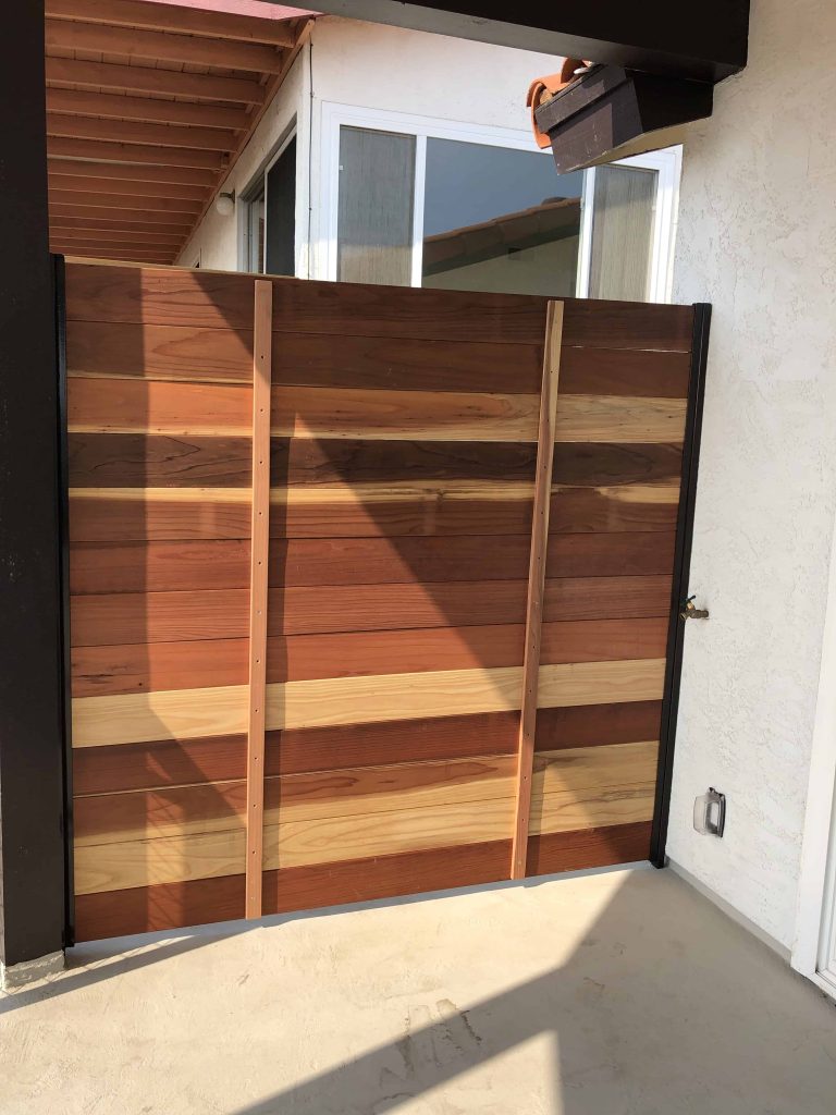 Horizontal wood plank privacy gate built on a metal frame beside a stucco home