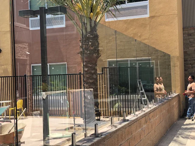 Crew installing tempered glass barrier panels on stainless spigots around a hotel pool deck