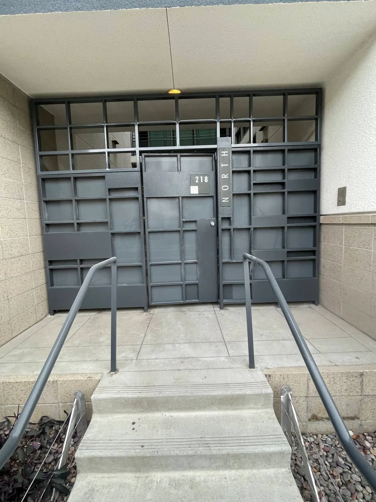 Charcoal steel commercial entry gate and screen wall in a square grid pattern at a building entrance with handrails