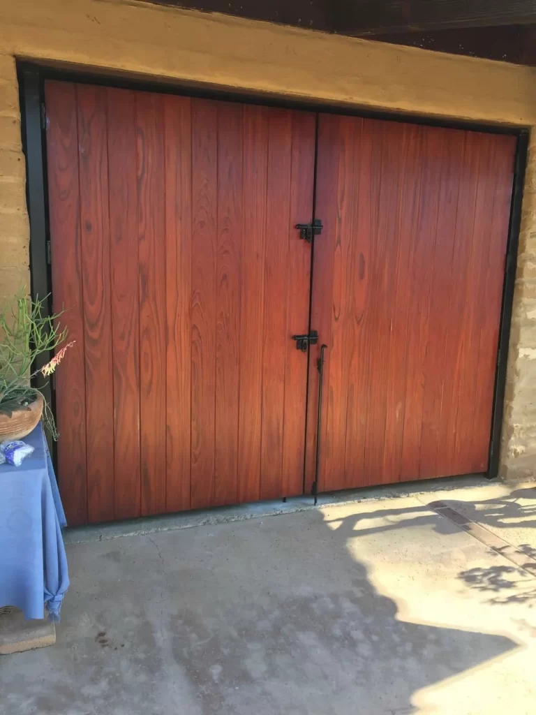 Stained wood double gate with two leaves set in a black steel frame across a wide side-yard opening