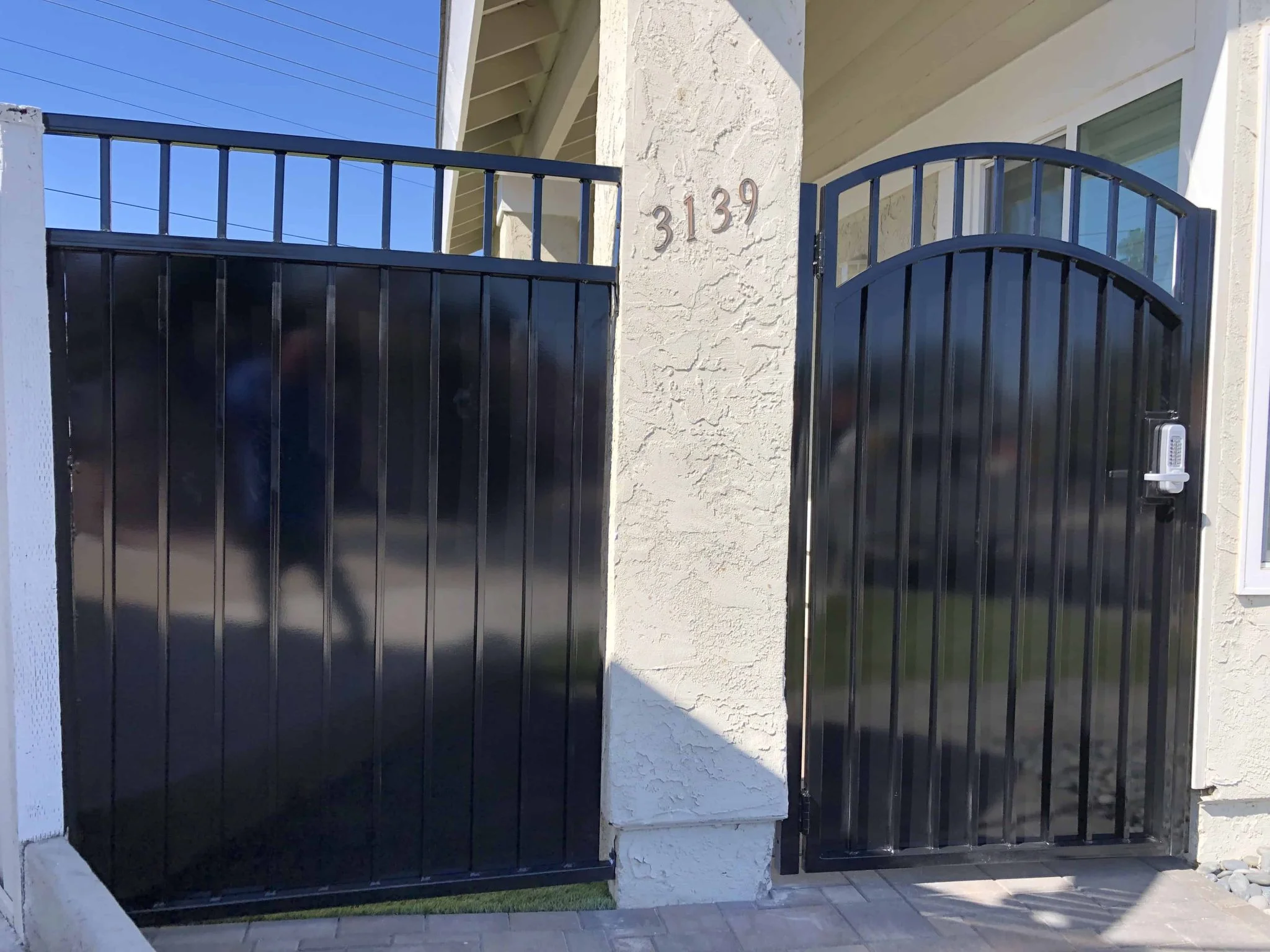 Black steel privacy panel with solid infill beside an arched-top iron pedestrian gate at a stucco home