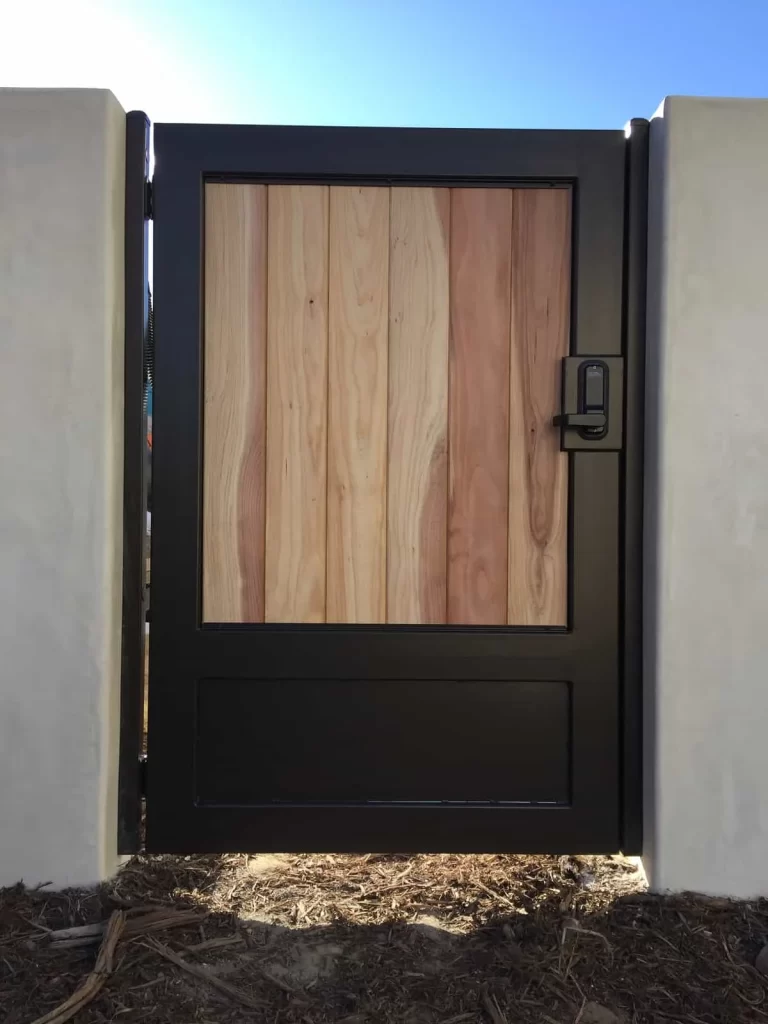 Black steel pedestrian gate with a natural wood upper panel, solid lower panel and keypad lock between stucco pillars