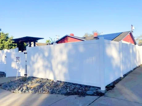 Solid white vinyl privacy fence and gate wrapping a corner lot, with a full-height gate beside a pergola
