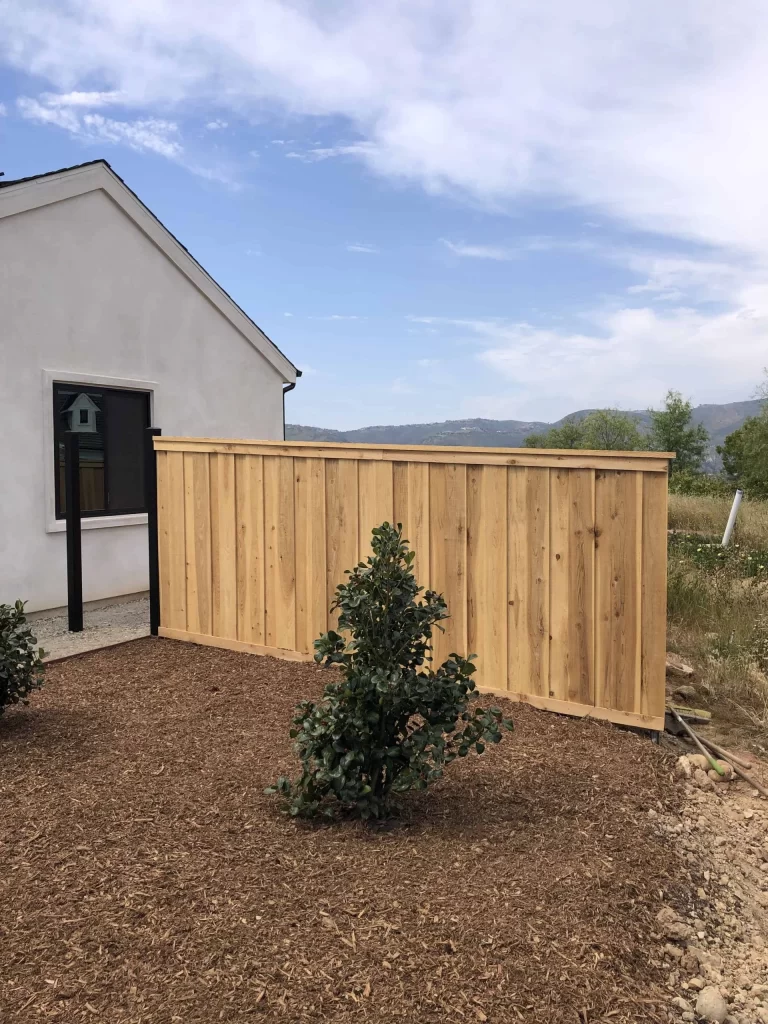 New cedar board fence run set into fresh mulch beside the corner of a home