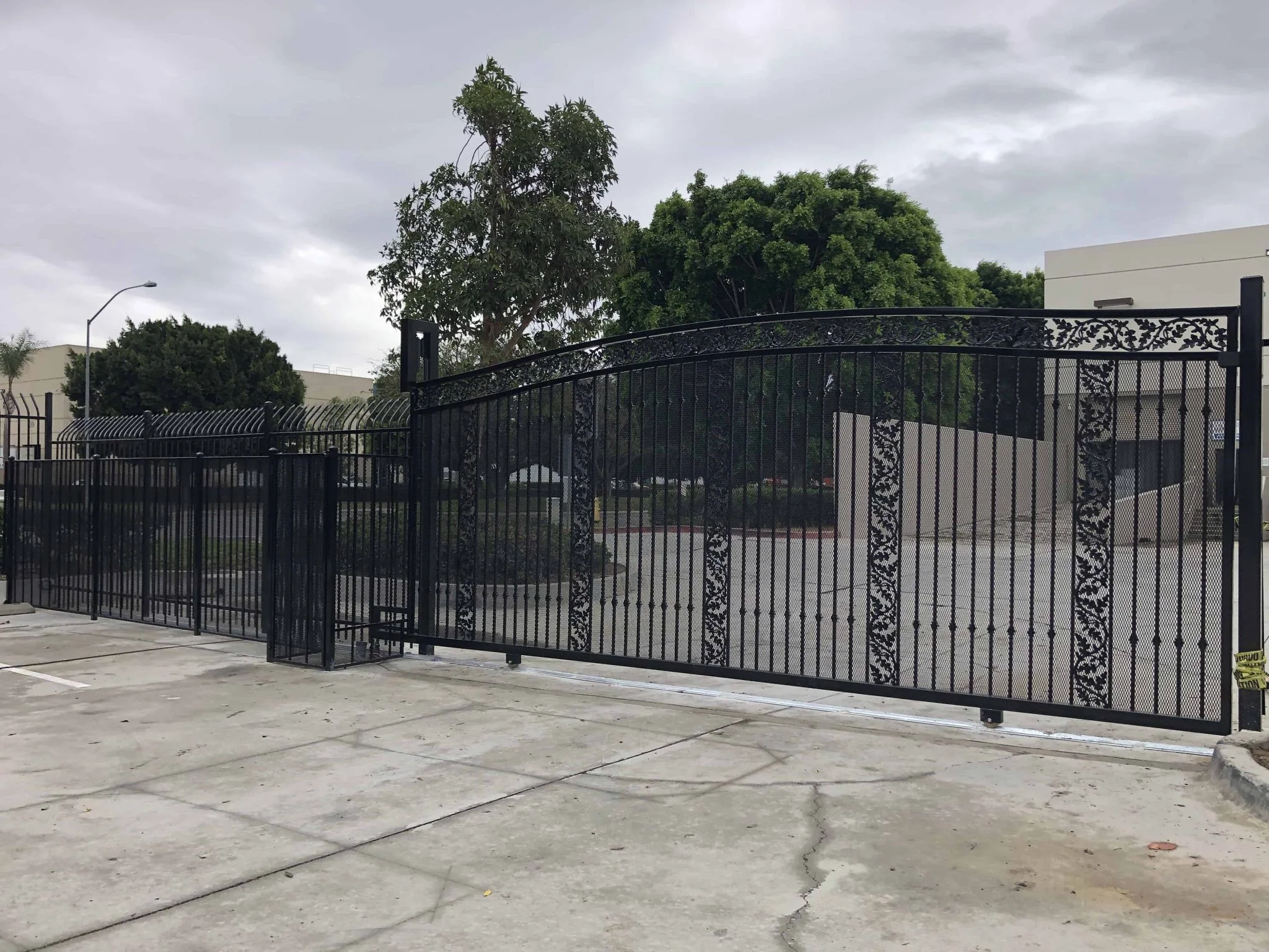 Wide ornamental black iron sliding gate with decorative scroll panels across a broad commercial entry