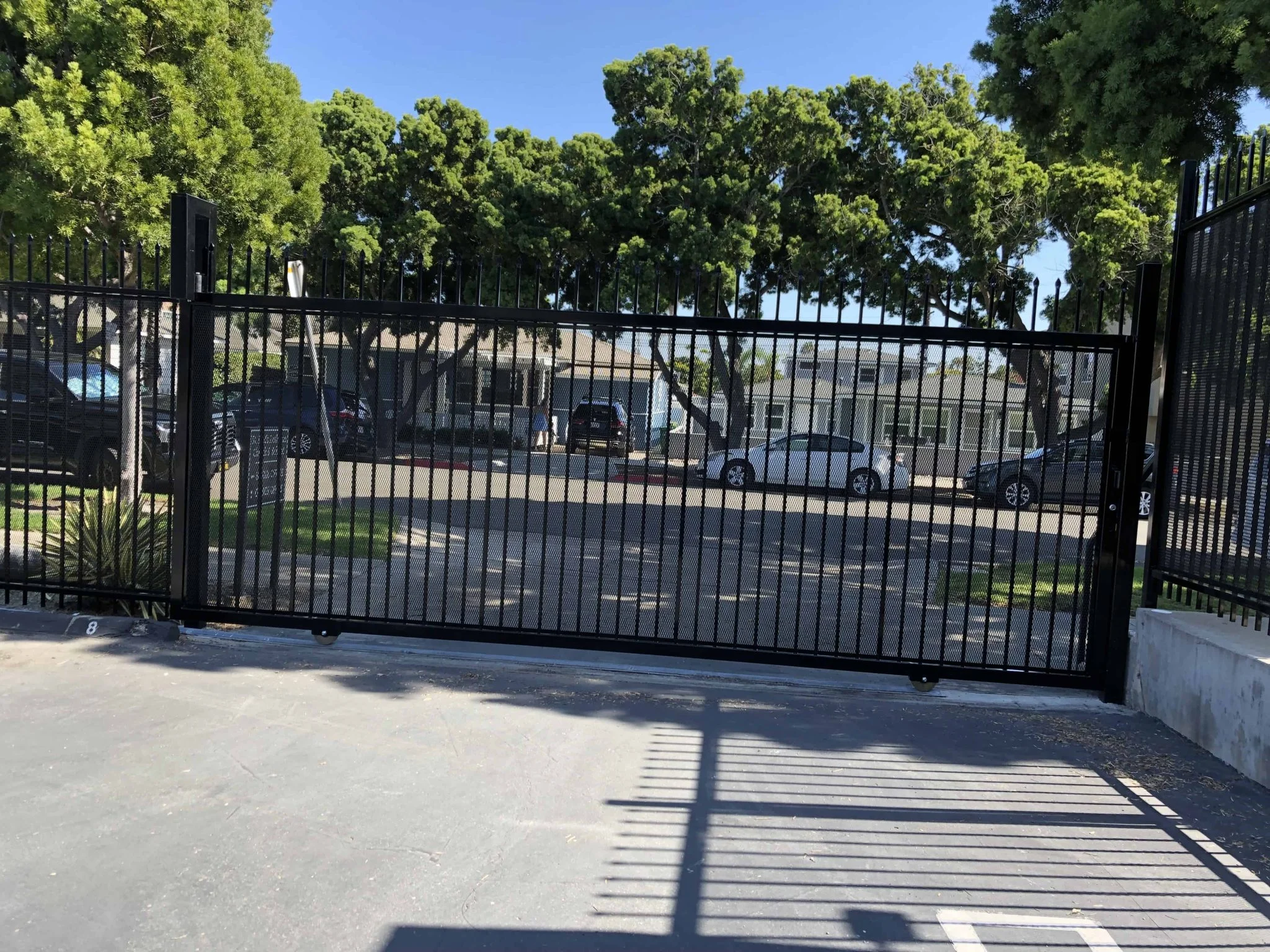 Black steel picket sliding gate securing a shared residential parking lot