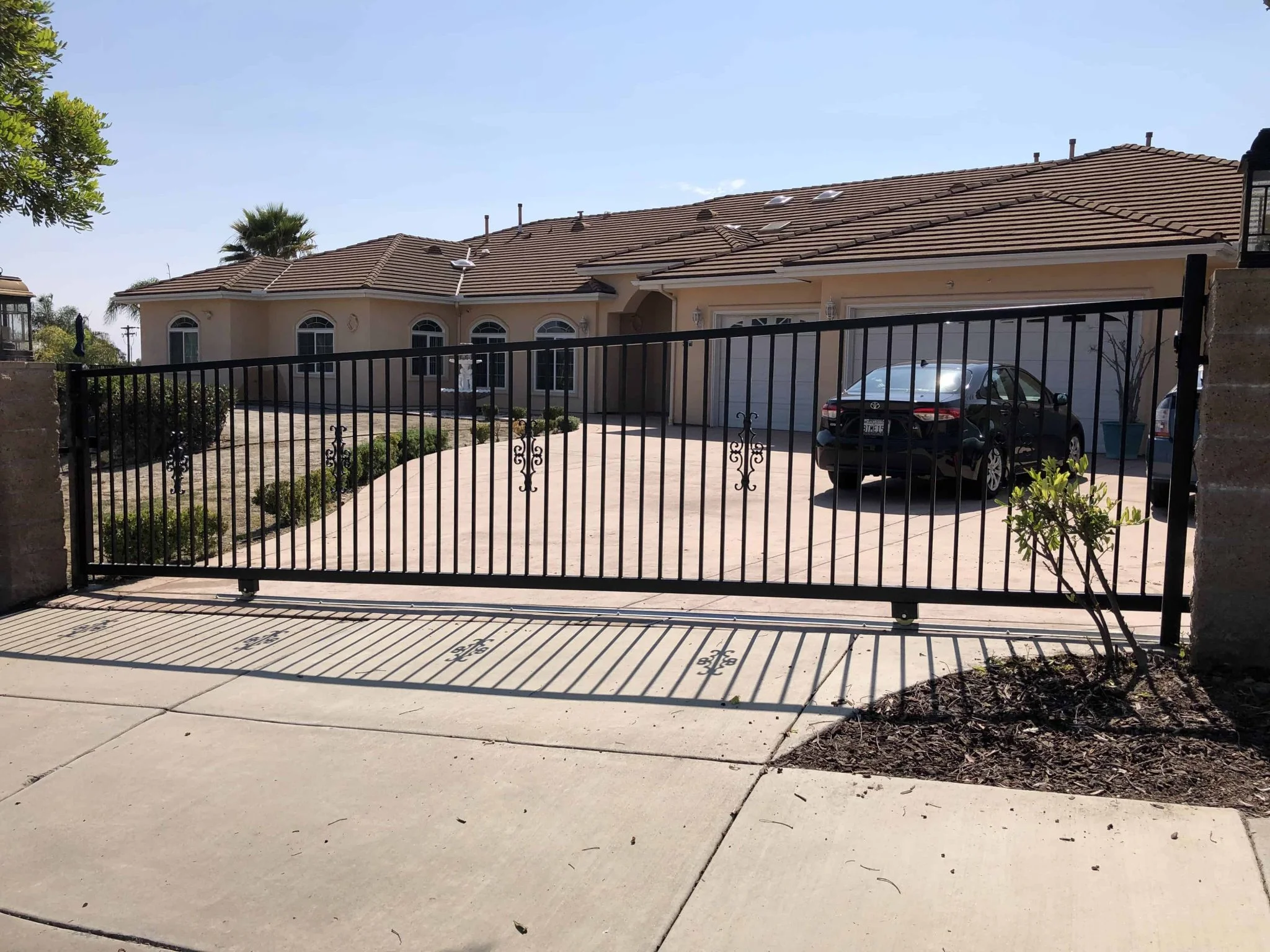 Black steel picket sliding gate closed across a wide residential driveway with a car parked just inside