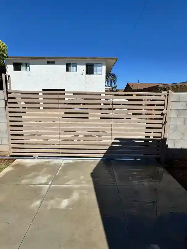 Tan horizontal-slat privacy sliding gate with a steel frame set between block walls