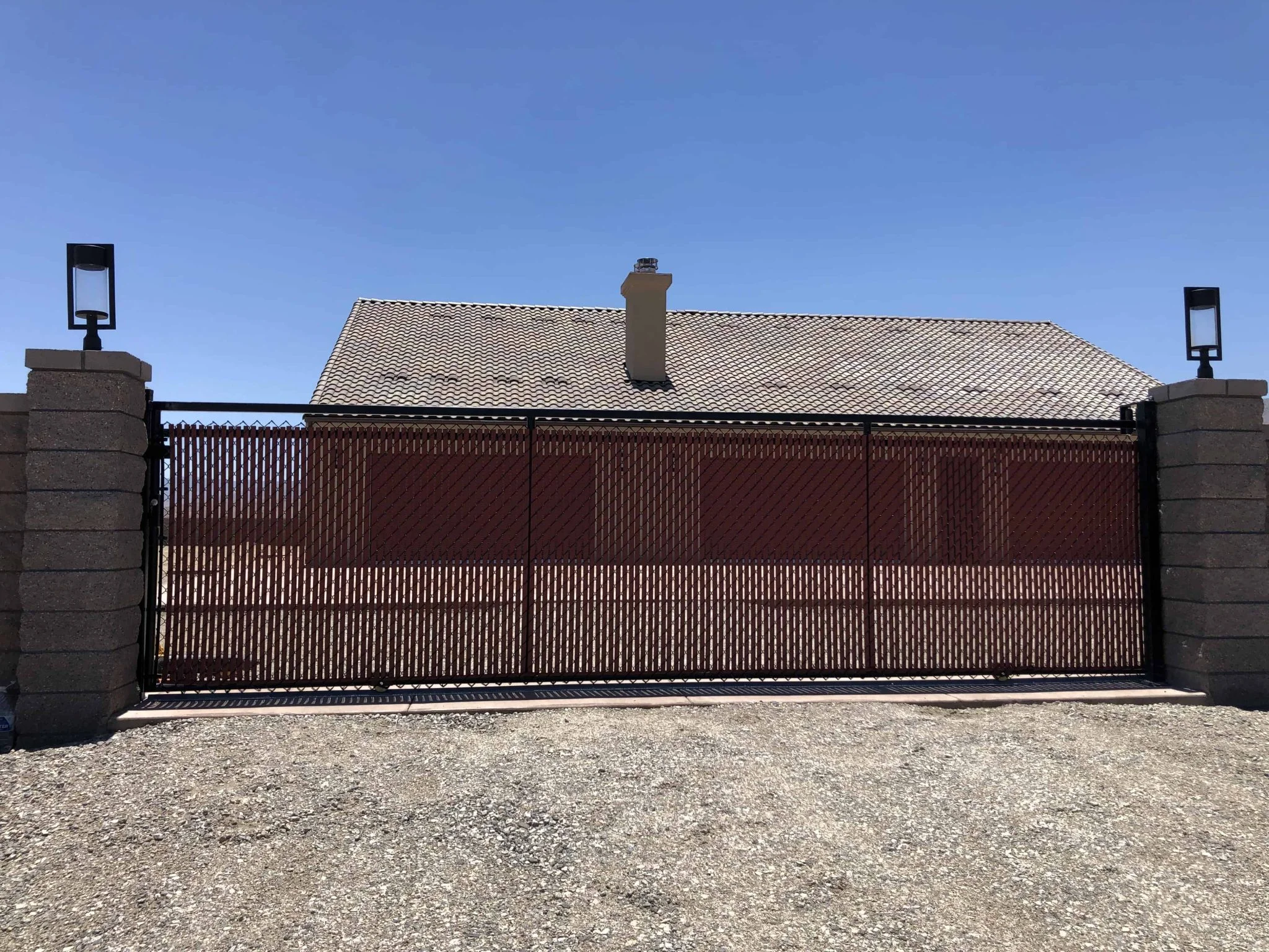 Wide steel sliding gate with privacy mesh infill between block pillars on a gravel lot