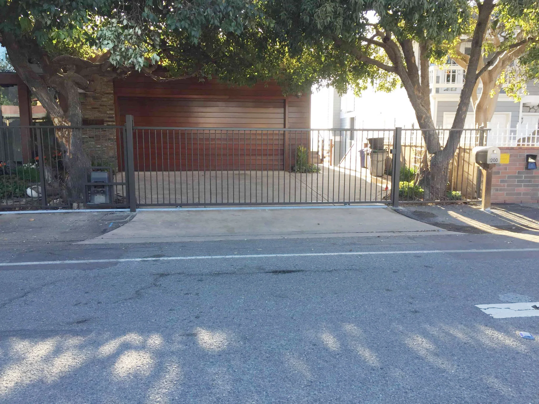 Black steel sliding gate at a short-setback driveway beside the street under mature trees