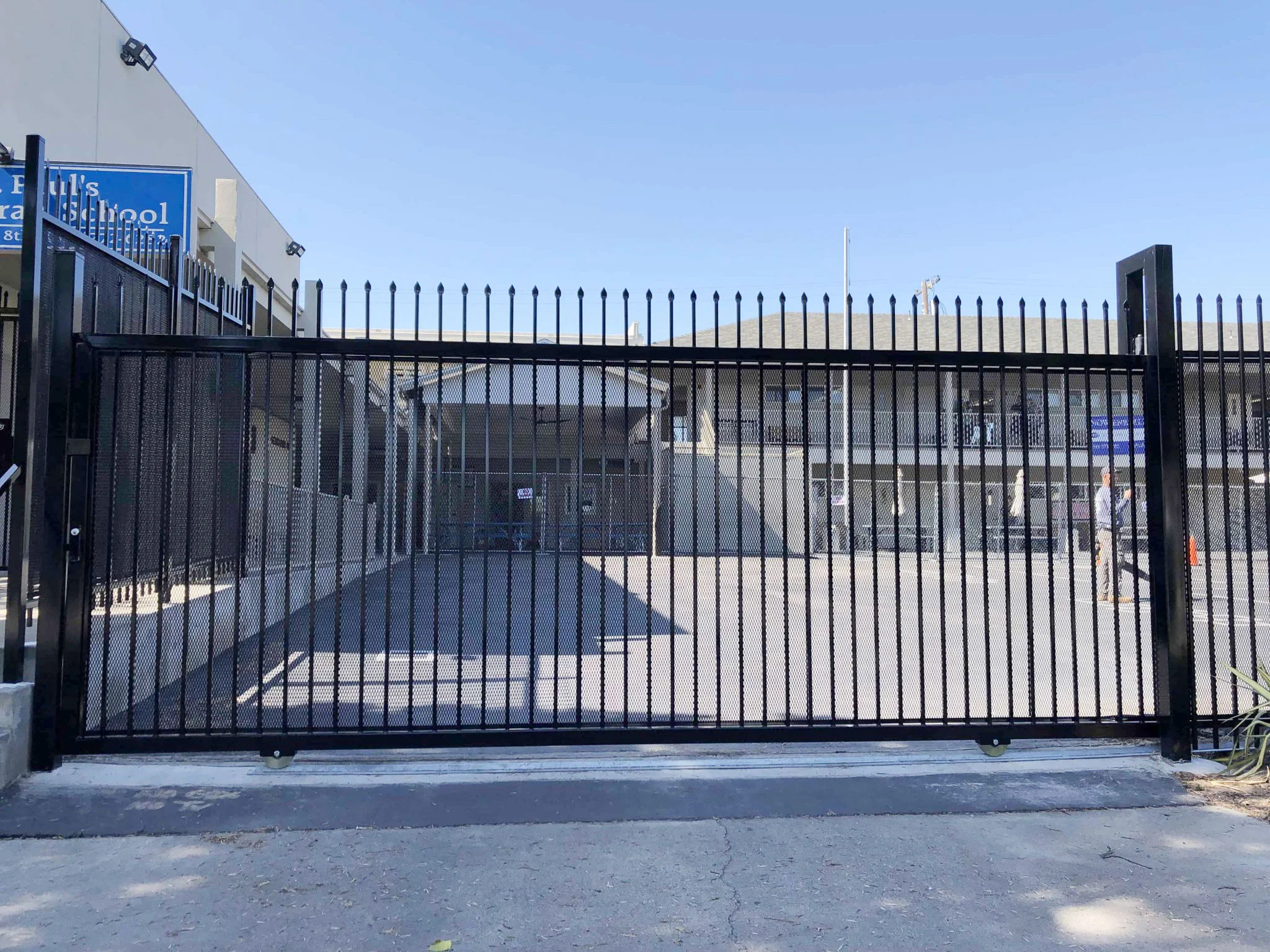 Tall black steel picket sliding gate securing a school campus entrance